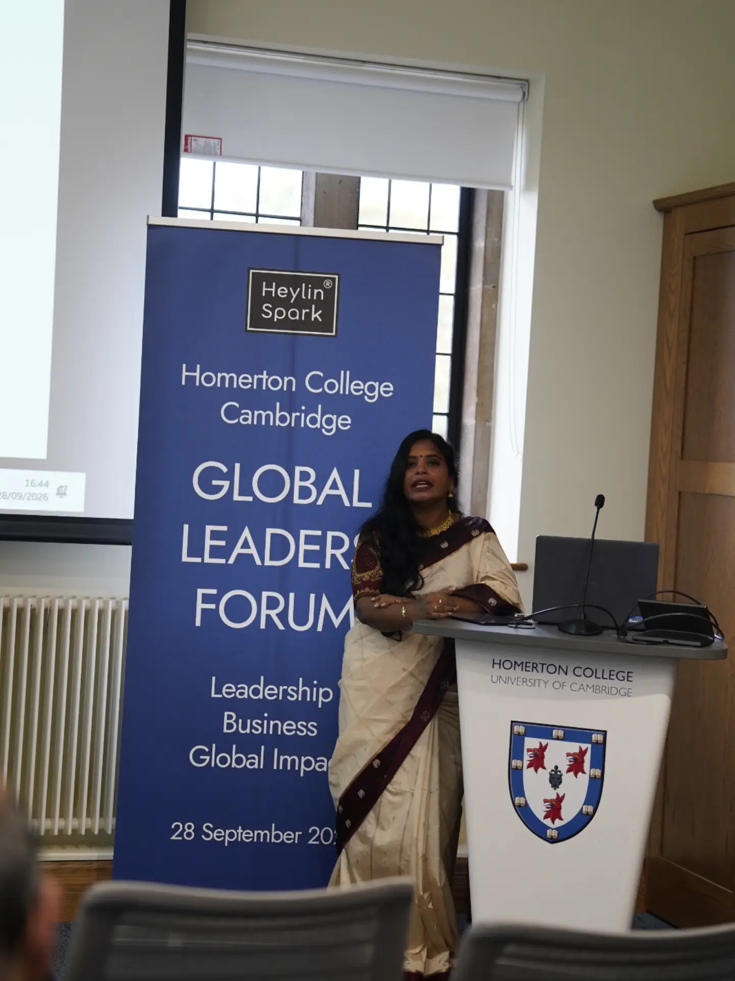Dr. Senbagam Raja speaking at the lectern at Homerton College, University of Cambridge